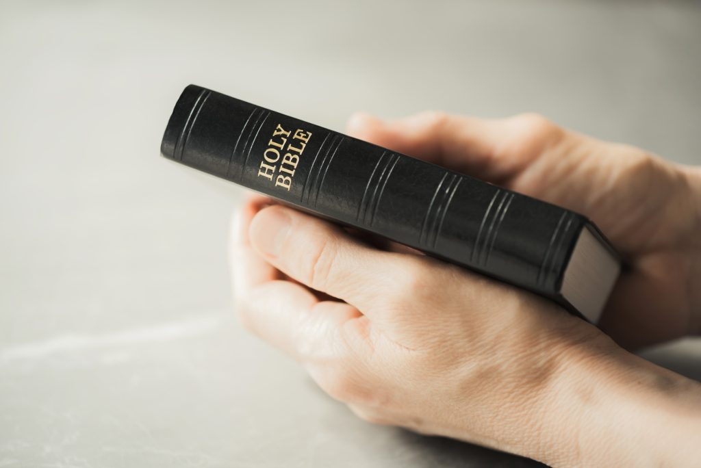 Hands holding Holy Bible over grey background. Sharing the Gospel with youth. Copy space. Christian